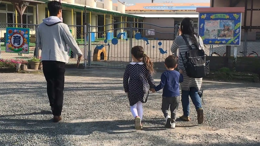 A guide with a mother and two young children outside the gates of a primary school.