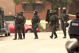 Several heavily armed police officers on a street, with guns and shields