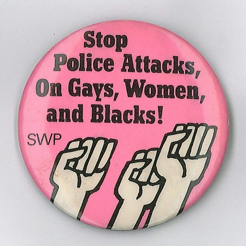 A pink coloured badge featuring illustration of three black raised fists.