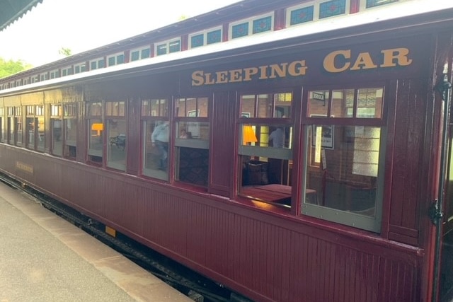 a red, olden railway car is lined up at a train platform
