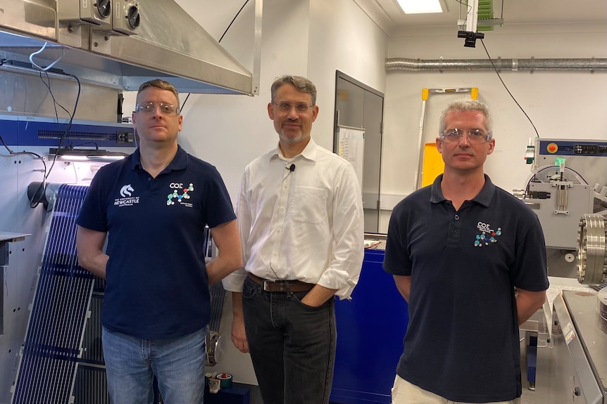 Three men standing in lab near printer