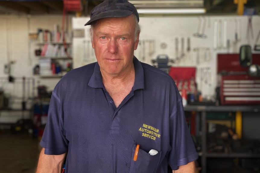 A man in a cap stands in a mechanic's workshop