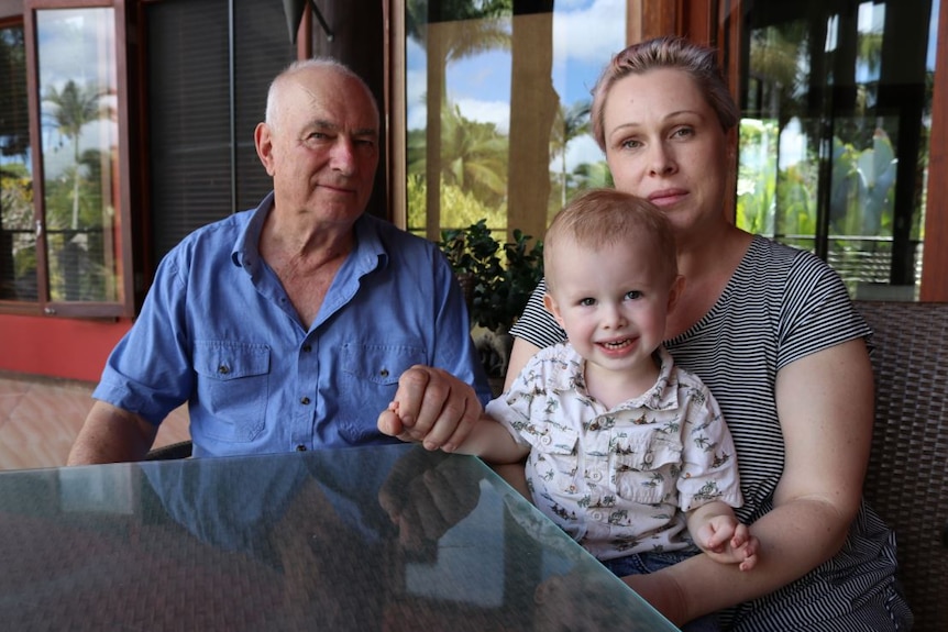 Ron Rutland sitting at a table on his deck with his daughter Amanda Rutland and smiling 22-month-old grandson Naish Dodson.