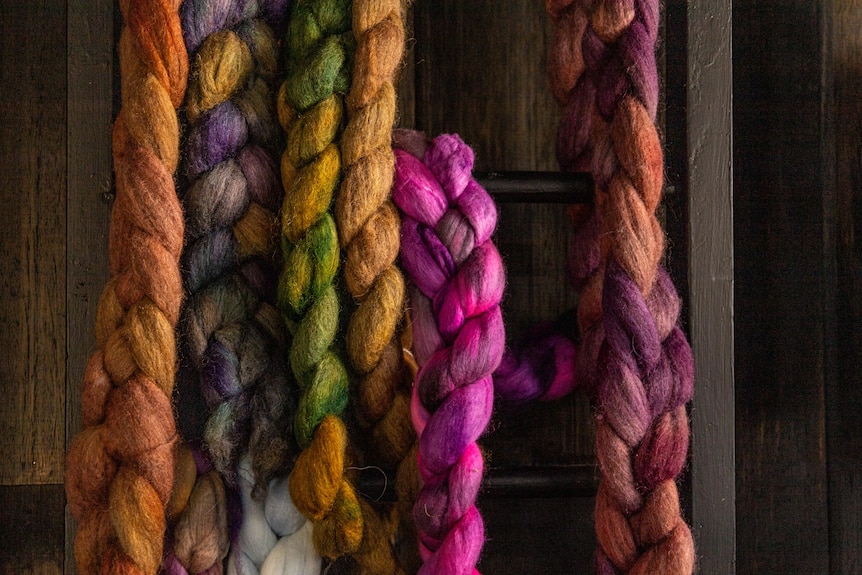Coloured wool in long plaits hang on a wall