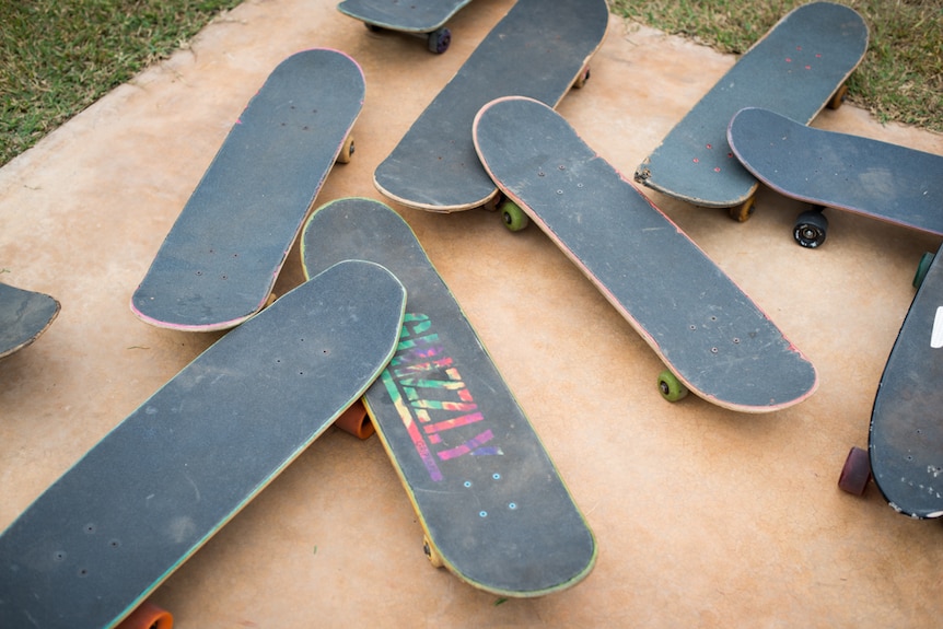 A collection of skateboards on a red-dirt stained concrete slab.