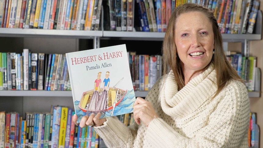 Female teacher holds book titled "Hebert & Harry"