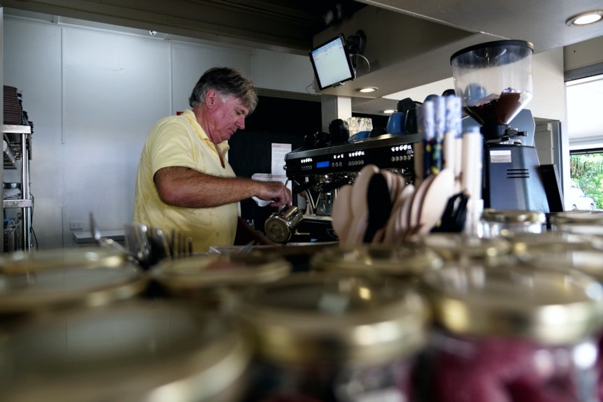 a man in a yellow polo shirt makes a coffee at a barista machine in a cafe