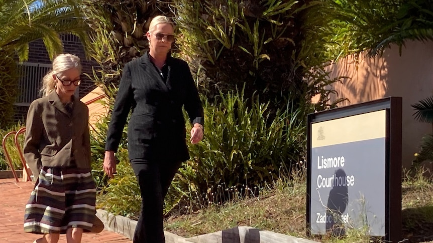 A blonde woman in a back outfit walks past a Lismore Courthouse sign