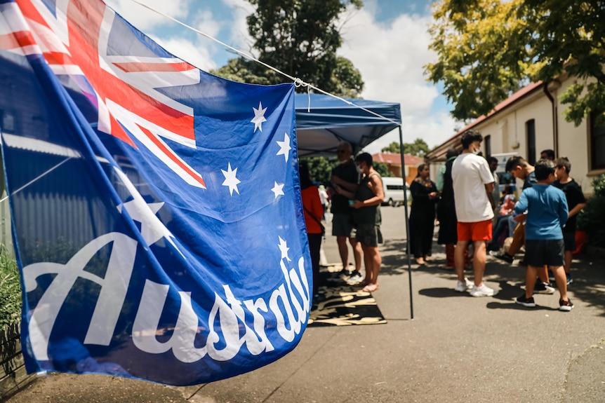 people in a yard for a barbecue next to a large australian flag