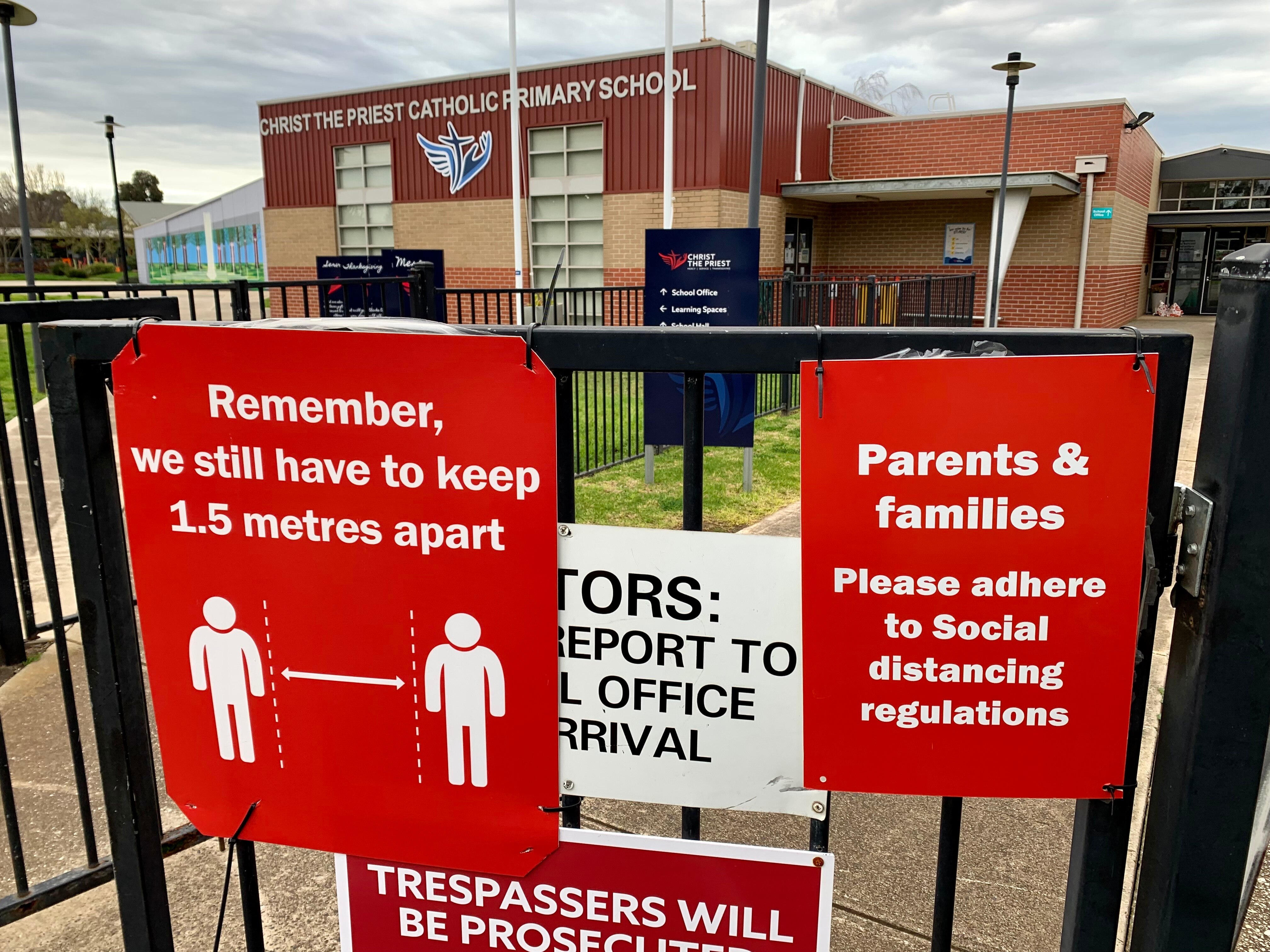 Red signs with warnings about social distancing are posted on the gate of the closed and empty primary school.