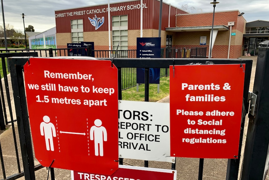 Red signs with warnings about social distancing are posted on the gate of the closed and empty primary school.