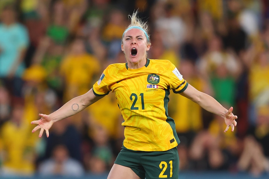 A Matildas player roars in celebration with arms spread wide after scoring a penalty.