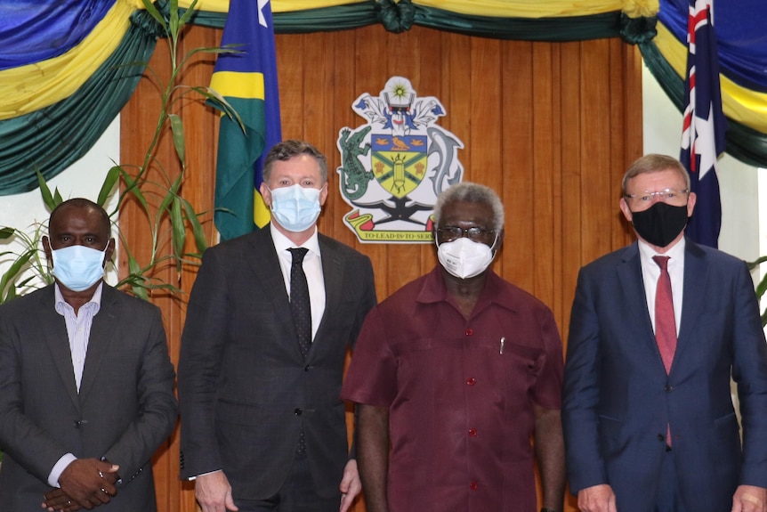 Six masked men stand for photo in front of Solomon Islands and Australian flags.