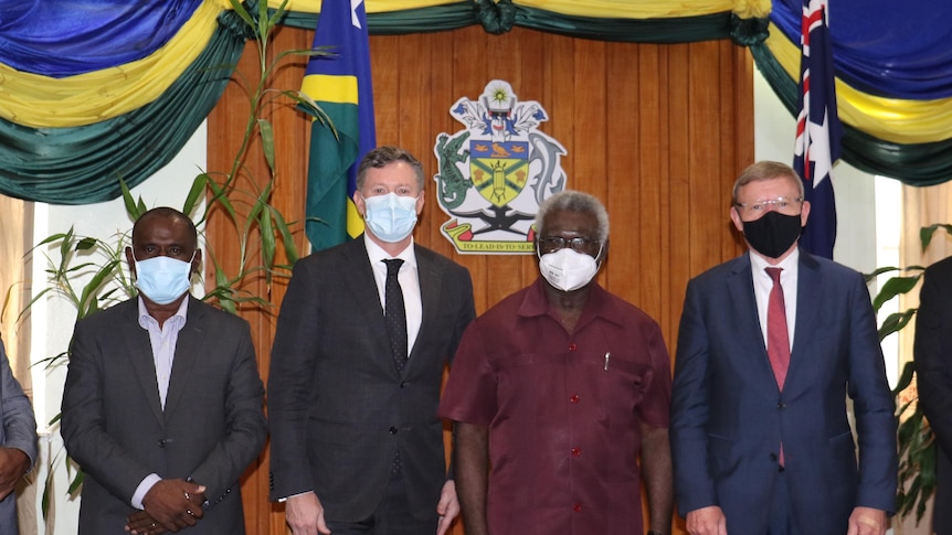 Six masked men stand for photo in front of Solomon Islands and Australian flags.