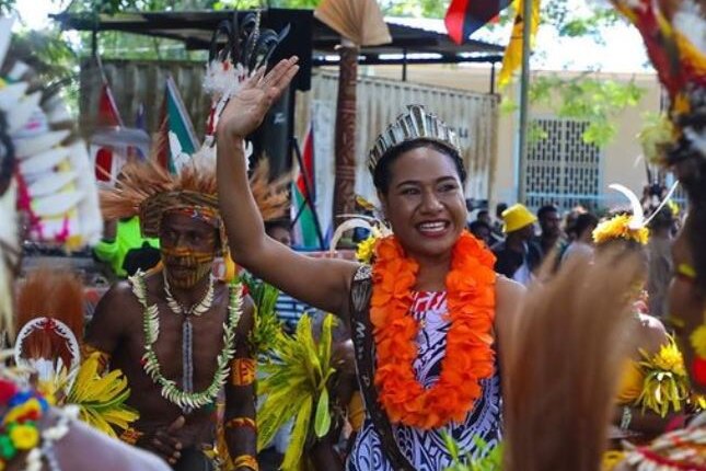 Beauty queen Josie Nicholas in bright orange lei surrounded by people dressed in traditional PNG attire. 