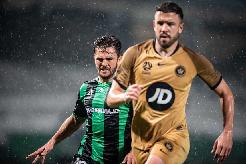 Steven Lustica of Western United and a Western Sydney Wanderers player chase the ball in the rain during an A-League match.