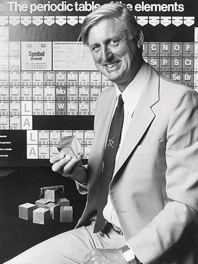 Mike Gore sits in front of the periodic table