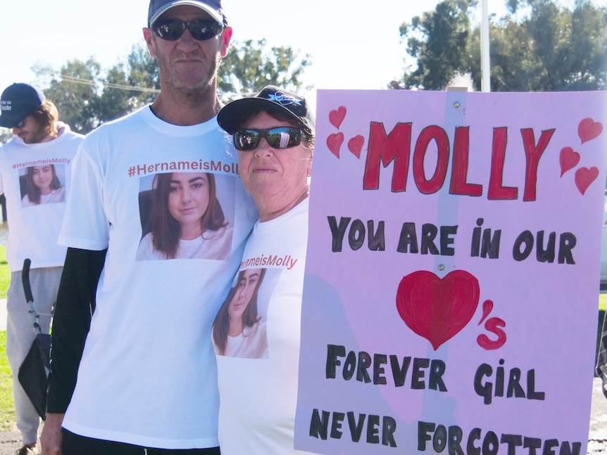 A man and a woman holding a placard saying "Molly you are our forever girl, never forgotten".