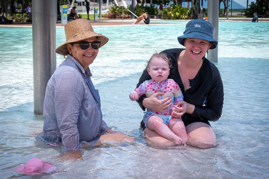 Two women sit in a pool with a baby girl