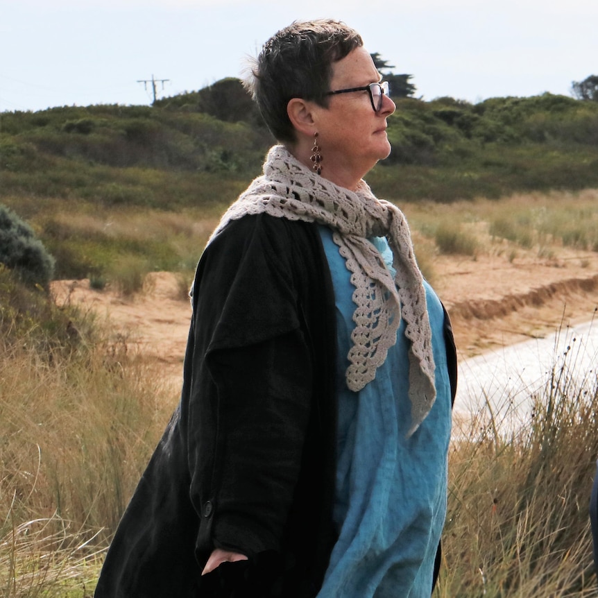 A woman stands on sandy banks of an estuary