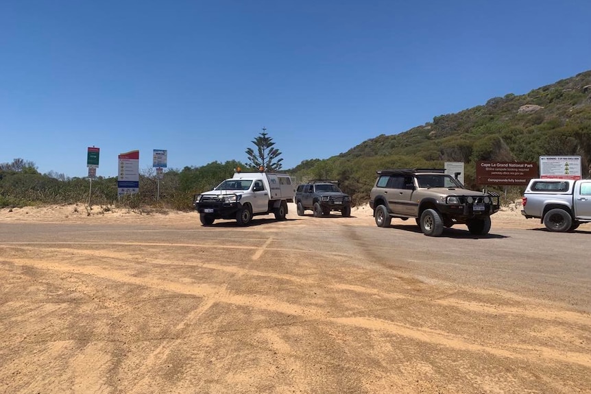 Vehicles drive off a sandy beach.