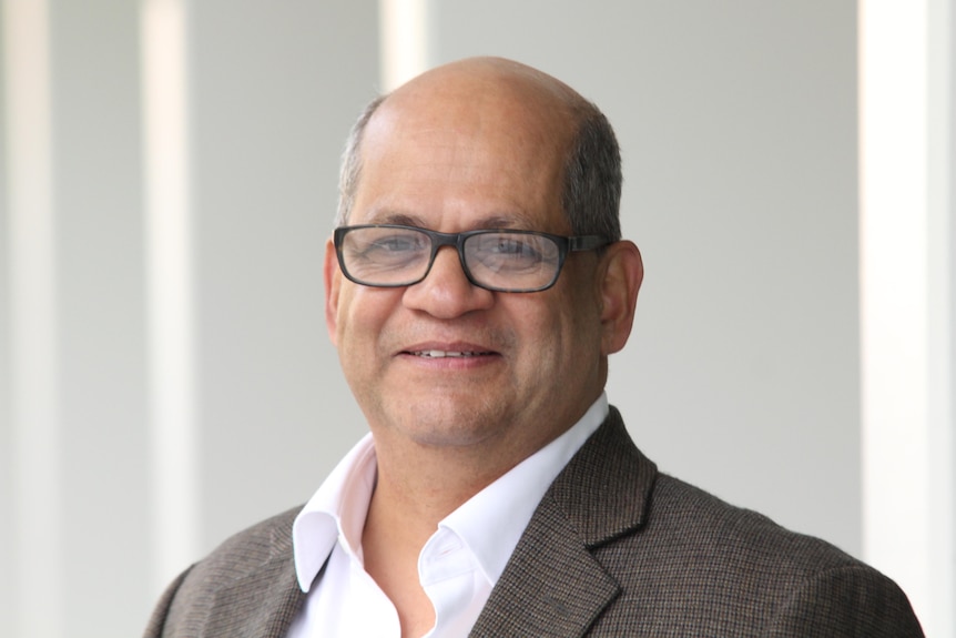 A headshot, he wears glasses and wears a jacket