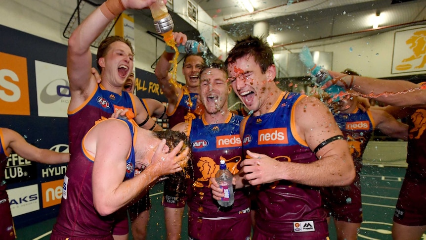 Four Lions players are covered in Gatorade as they stand in the middle of a huddle, singing the team song.