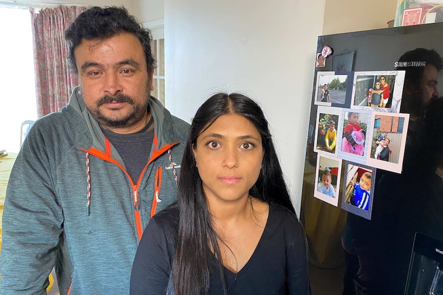 A couple stand at their fridge with pictures on it of their children.