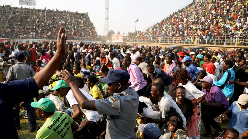 Looking across a rectangular stadium, you view a sea of people rushing across the pitch to the body of Robert Mugabe.