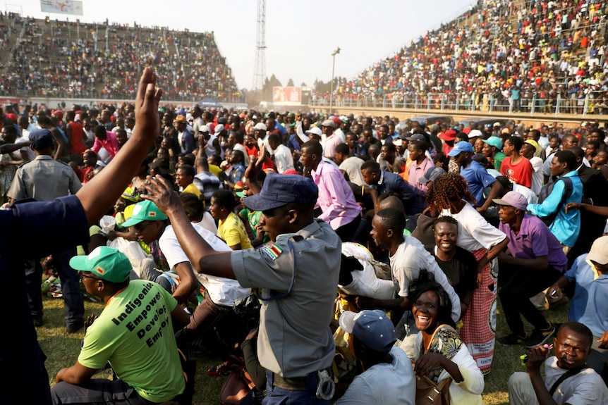 Looking across a rectangular stadium, you view a sea of people rushing across the pitch to the body of Robert Mugabe.