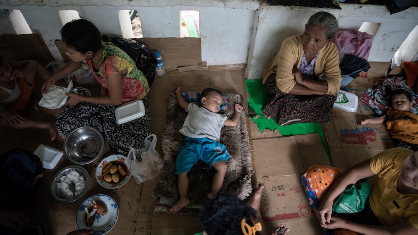 A baby sleeps on the floor as families eat nearby. 