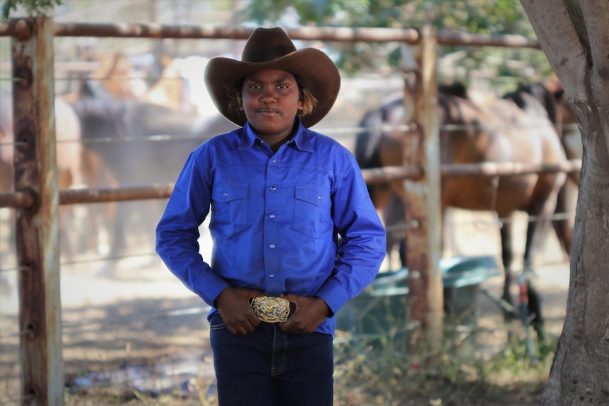 A young Aboriginal boy wearing bright blue shirt and cowboy hat with his hands on hips.