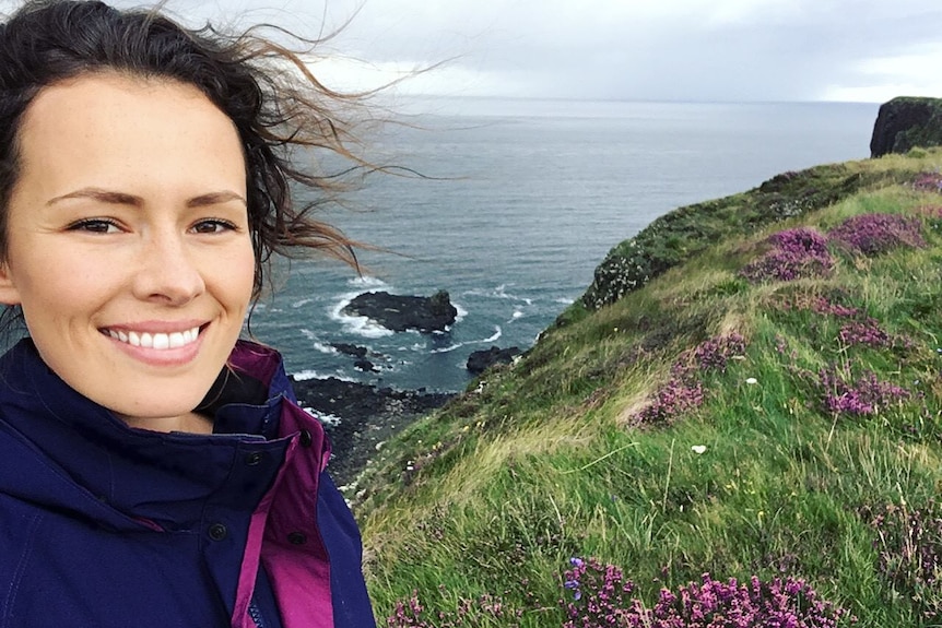 Selifie of a young woman on a picturesque cliffside overlooking the ocean.