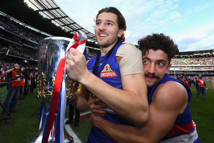 Marcus Bontempelli holds the premiership cup as Tom Liberatore hugs him from behind
