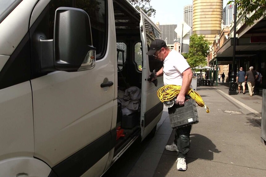 Andrew Klohk closes the door of his work van on a Sydney city street, holding an armful of tools and electrical cords