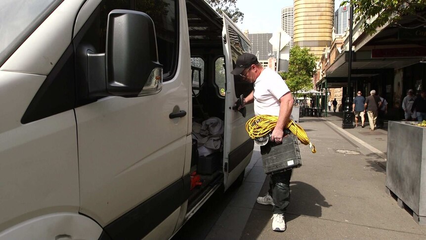 Andrew Klohk closes the door of his work van on a Sydney city street, holding an armful of tools and electrical cords