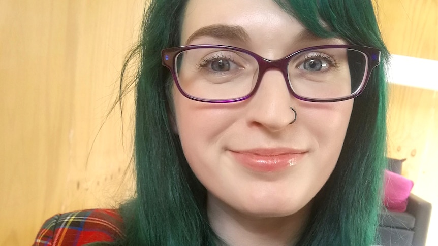 A young woman with emerald green hair and glasses smiles