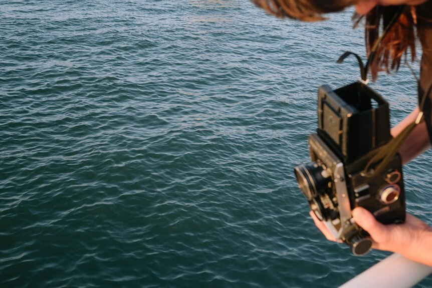 Photographer Sammy Hawker holds a medium format camera, photographing the surface on Sydney Harbour 