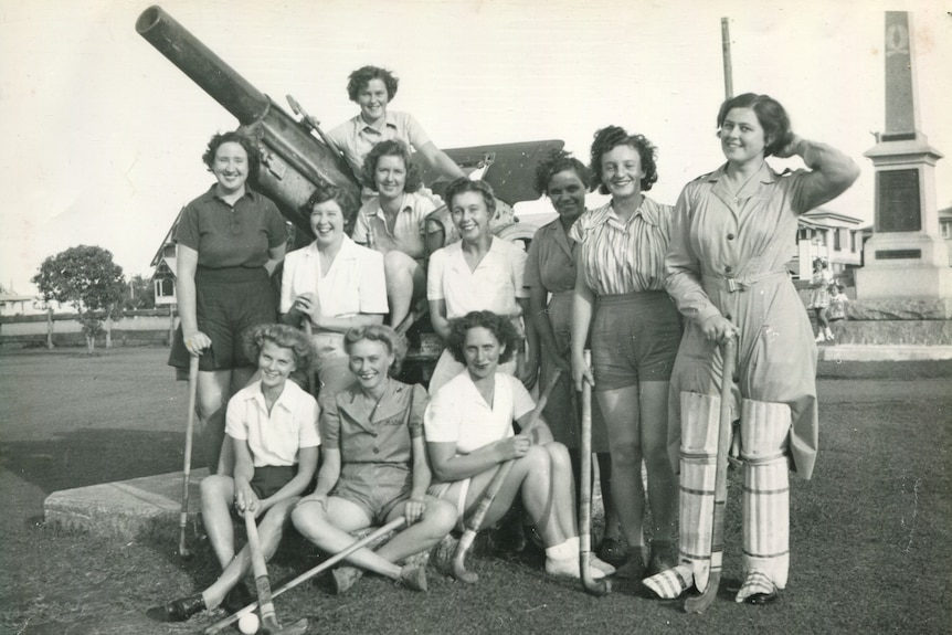 A smiling group of girls with hockey sticks and knee pads