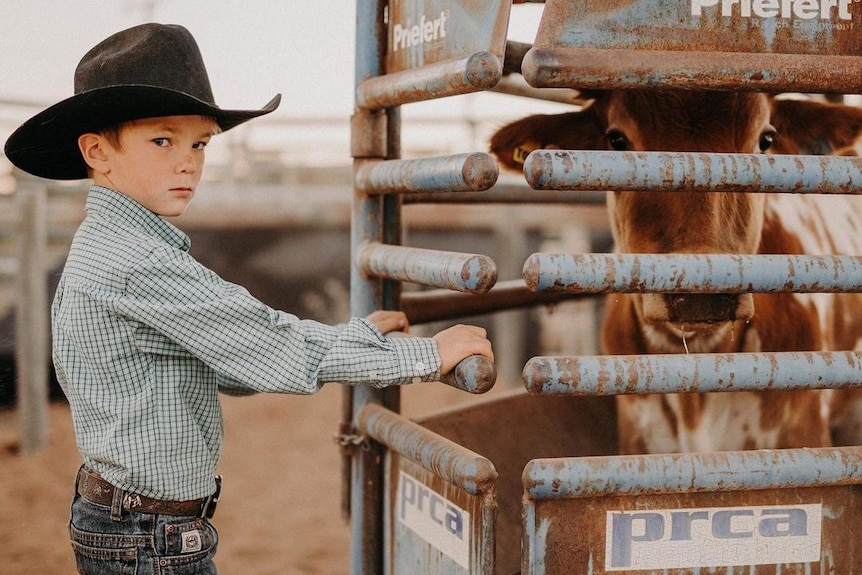 A young bow wearing a black cowboy hat looks at the camera seriously