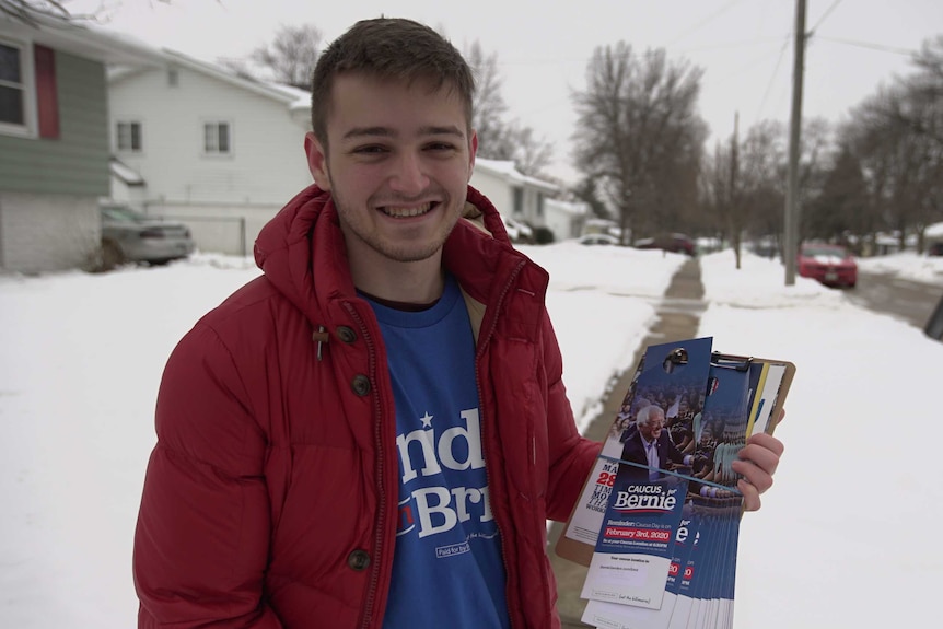 A guy in a Bernie Sanders t-shirt standing on a snowy street holding pamphlets