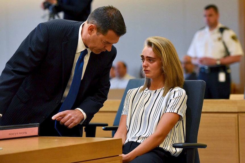 A man in a suit bends over to speak to a distressed young woman in court.