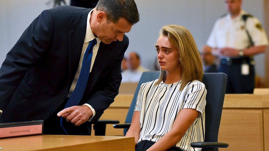 A man in a suit bends over to speak to a distressed young woman in court.