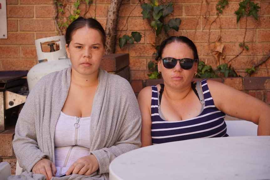 Two women sit in a courtyard posing for a photo.