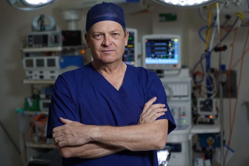 Man wearing blue scrubs standing in a hospital.