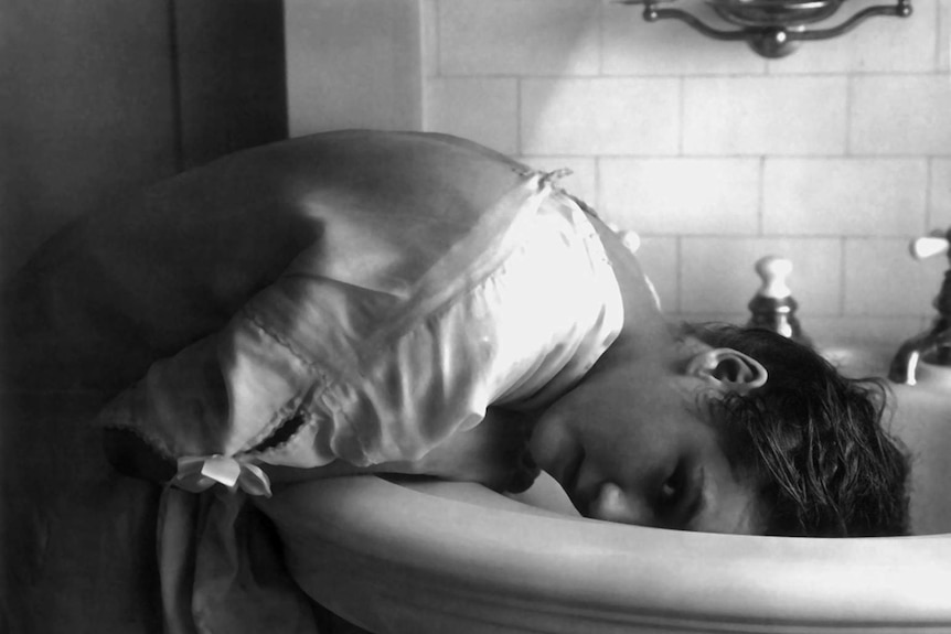 A black and white photo of a woman in 1922 leaning over a sink to wash her hair.