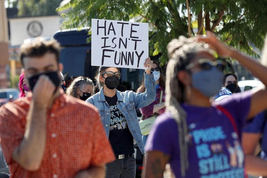 Protesters march while one holds a sign readin "Hate isn't funny".