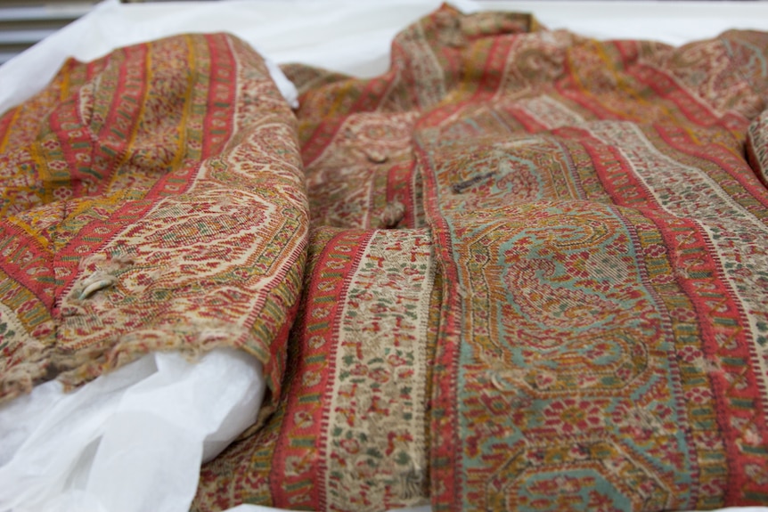 A worn paisley dressing gown woven from orange, red, white and green.