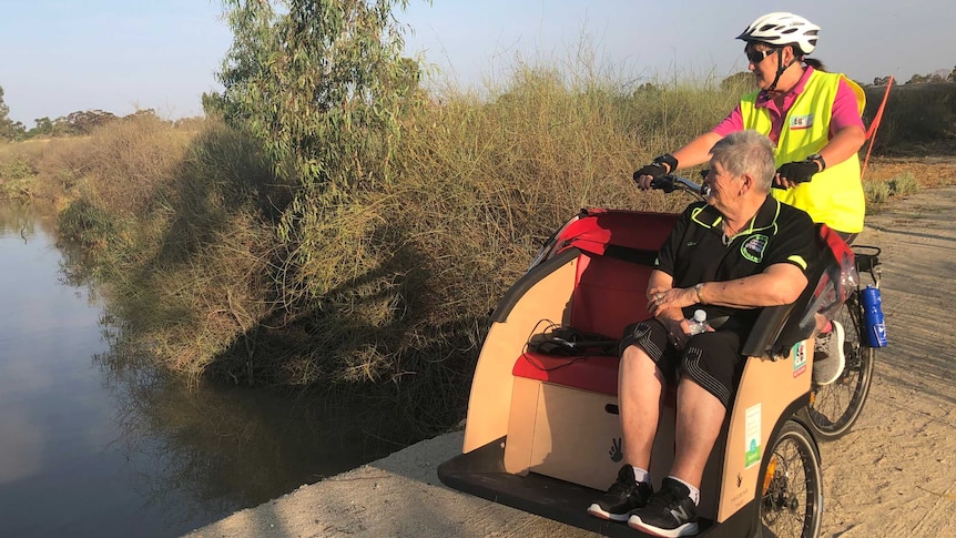 A lady sits on a special seat at the front of a bike that is being ridden by another lady they are looking at a wetland