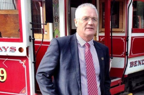 A man in a suit stands in front of a tram